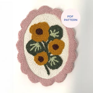 Puede incluir: Un patrón floral de aguja mágica con un borde festoneado rosa. El diseño presenta flores amarillas con centros marrones y hojas verdes, sobre un fondo blanco. El texto "PDF PATTERN" está en un círculo blanco.