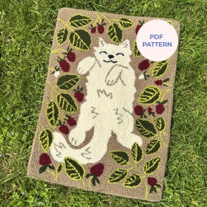Puede incluir: Alfombra beige con un diseño de gato blanco sonriente, rodeado de hojas verdes y bayas rojas. La alfombra tiene un borde marrón y el texto "PDF PATTERN" en un círculo blanco.