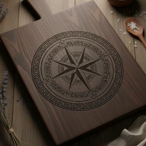May include: A dark brown wooden cutting board with a handle. The board features an engraved compass rose design in the center. The compass rose is surrounded by decorative patterns. The board is rectangular and appears to be made of hardwood.