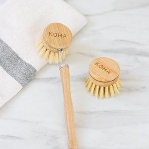 May include: Two wooden dish brushes, one with a long handle and a replacement head. The word "KOHA" is printed on the top of each brush. The bristles are light-colored. The handle has a metal loop.