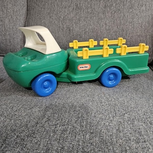 Puede incluir: Un cami&oacute;n de juguete Little Tikes verde y blanco con ruedas azules. El cami&oacute;n tiene un remolque con detalles amarillos en forma de valla. El cami&oacute;n de juguete est&aacute; dise&ntilde;ado para ni&ntilde;os y est&aacute; hecho de pl&aacute;stico duradero.