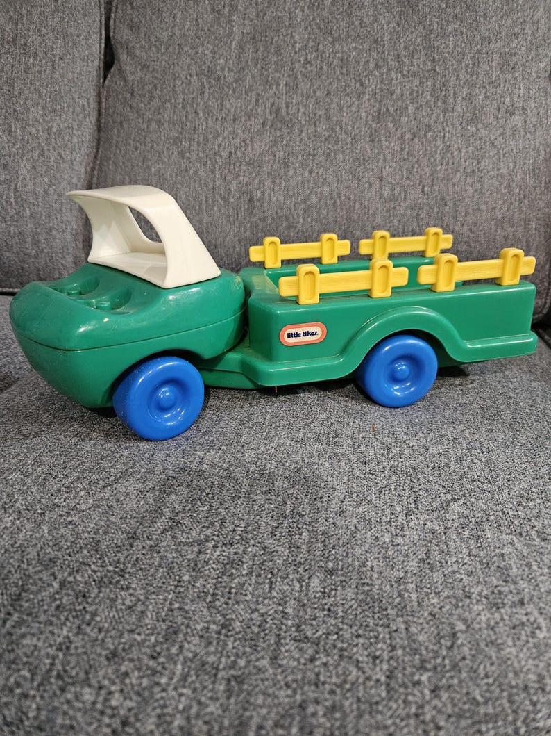 Puede incluir: Un cami&oacute;n de juguete Little Tikes verde y blanco con ruedas azules. El cami&oacute;n tiene un remolque con detalles amarillos en forma de valla. El cami&oacute;n de juguete est&aacute; dise&ntilde;ado para ni&ntilde;os y est&aacute; hecho de pl&aacute;stico duradero.