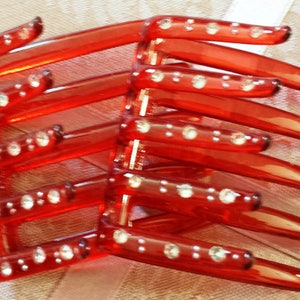May include: A red hair comb with a series of teeth, adorned with small, sparkling rhinestones. The comb is made of a translucent, glossy material, and the rhinestones are evenly spaced along the comb's teeth.
