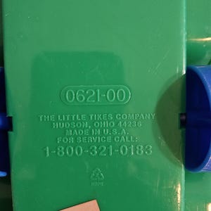 Puede incluir: Primer plano de un componente de juguete de pl&aacute;stico verde con el texto "0621-00". Tambi&eacute;n se ve el texto "THE LITTLE TIKES COMPANY" y un n&uacute;mero de tel&eacute;fono. Una peque&ntilde;a pegatina con el texto "H7J012" est&aacute; adjunta.
