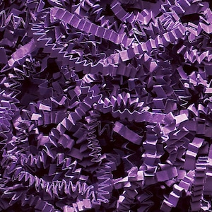 Può includere: Primo piano di carta crespa viola, un materiale di imballaggio decorativo. La carta è tagliata in lunghe strisce a zig-zag, creando un effetto strutturato e visivamente interessante. Il colore è un viola intenso e saturo, adatto per confezioni regalo o riempimento di cesti.