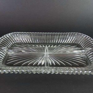 Puede incluir: Un plato de servir de vidrio transparente con cuatro secciones. El plato tiene un borde en forma de diamante y un patrón de estrella en la parte inferior.