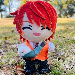 May include: A plush doll with red hair, wearing an orange vest, white shirt, and black boots. The doll has a small, smiling face and is carrying a blue bag with a white bunny. The doll is standing in a grassy area.