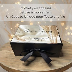 Peut inclure: Un coffret noir avec un couvercle blanc portant l'inscription "Lettres à Fanny" et "Un message pour la vie...". La boîte est nouée avec un ruban noir. Le couvercle porte également l'inscription "Coffret personnalisé Lettres à mon enfant Un Cadeau Unique pour Toute une Vie."