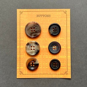 May include: A card with the word "BUTTONS" printed on it. Six buttons are displayed on the card. Three buttons are brown with black speckles and four holes. Three buttons are black with four holes.
