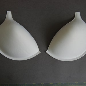 May include: Two white foam bra cups, designed to add volume and shape to a bra.