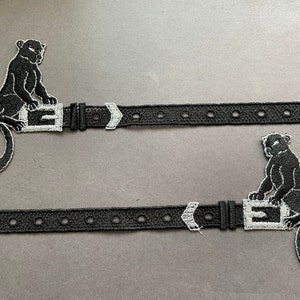以下が含まれることがあります： 銀色のバックルと黒いパンサーの刺繍が施された黒い革のベルト2本。各ベルトにはサイズ調整用の穴が5つあります。