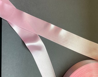 Könnte beinhalten: Eine Rolle pinkfarbenes Satinband auf grauem Hintergrund. Das Band ist aufgerollt und das Ende des Bandes liegt auf der Oberfläche.