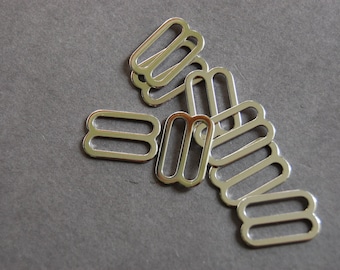 May include: A group of silver metal slider buckles, commonly used for adjusting straps on clothing or bags.