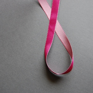 May include: A pink and light pink ribbon tied in a loop on a gray background.
