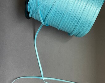 May include: A spool of light blue satin ribbon with a white stripe pattern. The ribbon is wound around a black spool and a length of ribbon is hanging down.