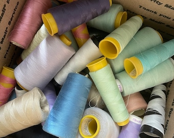 Op de afbeelding: Een doos gevuld met spoelen garen in verschillende kleuren, waaronder roze, paars, blauw, groen en wit. De spoelen zijn in een willekeurig patroon gerangschikt, met sommige spoelen die op elkaar gestapeld zijn.