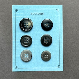 May include: Six black and gray buttons with four holes each, displayed on a light blue card with the word "BUTTONS" printed in black.