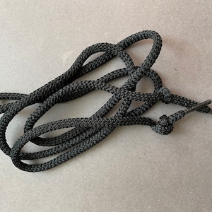 Puede incluir: Un cordón de zapato negro con un extremo anudado. El cordón está hecho de un material grueso y trenzado.