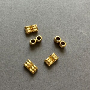 Puede incluir: Cinco cuentas de metal doradas con una superficie texturizada. Las cuentas son de varias formas, incluyendo redondas y rectangulares.