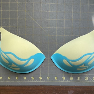 May include: Two light blue bra cups with a white flame design. The cups are made of foam and are ready to be sewn together.