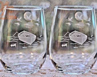 May include: Two clear glass wine glasses with an etched design of a boat, birds, and a turtle on a body of water. The design is in white and is visible on the front of each glass.