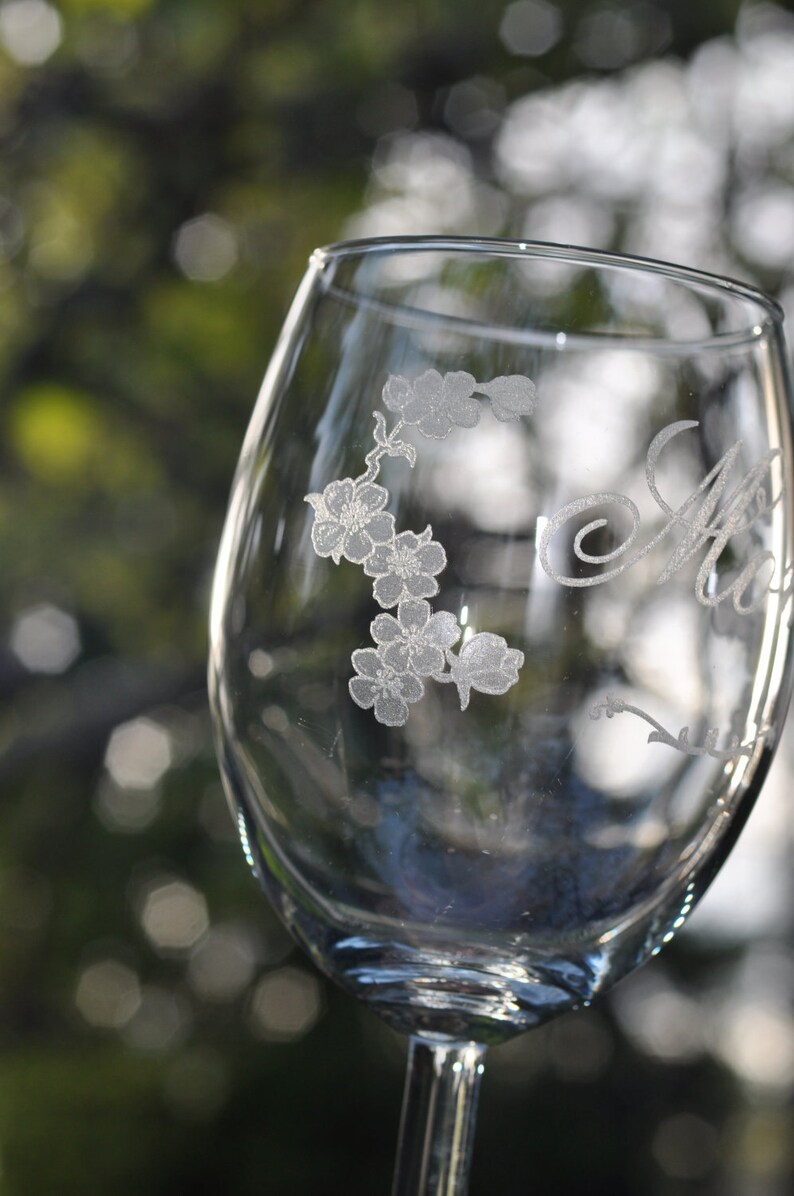 May include: A clear glass wine glass with an etched design of flowers and the word "Aunt" on the side.