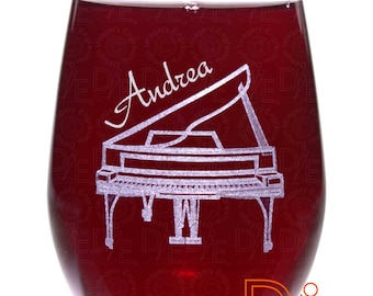 May include: A clear wine glass with a red liquid inside. The glass is engraved with a piano and the name "Andrea".