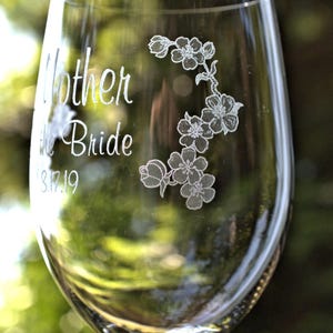 Könnte beinhalten: Ein klares Weinglas aus Glas mit einem gravierten Design einer Blumenranke und dem Text "Mother of the Bride 8.17.19".