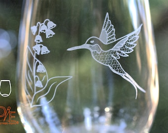 May include: A clear glass wine glass with an etched design of a hummingbird and lily of the valley flowers.