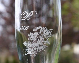 May include: A clear glass champagne flute featuring an etched design of a columbine flower cluster. The glass is engraved with the letter P in a cursive script and the year 2026 positioned below the letter, showcasing a smooth, transparent finish.