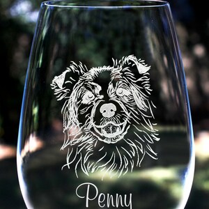 K&ouml;nnte beinhalten: Ein klares Weinglas aus Glas mit einem wei&szlig;en, ge&auml;tzten Bild eines Hundefaces und dem Namen "Penny" darunter.