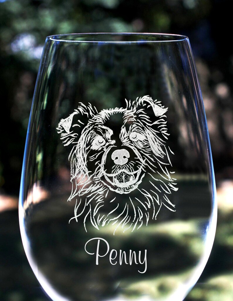K&ouml;nnte beinhalten: Ein klares Weinglas aus Glas mit einem wei&szlig;en, ge&auml;tzten Bild eines Hundefaces und dem Namen "Penny" darunter.