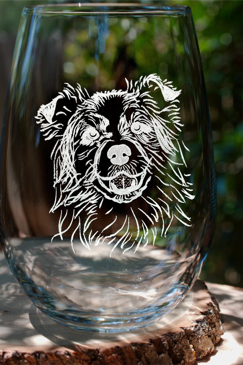 K&ouml;nnte beinhalten: Ein klares Weinglas aus Glas mit einem wei&szlig;en, ge&auml;tzten Design eines Hundegesichts. Der Hund hat schwarzes Fell und schaut direkt auf den Betrachter.