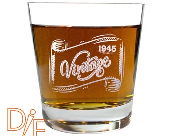 May include: A clear glass tumbler with a brown liquid inside. The glass has an etched design that says "Vintage 1945" in a decorative font.
