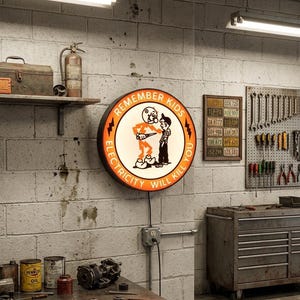 Può includere: Un'insegna circolare da parete con bordo arancione e centro bianco, raffigurante un'illustrazione a cartone animato di un personaggio a forma di fulmine e un bambino. Il testo recita REMEMBER KIDS ELECTRICITY WILL KILL YOU in nero.