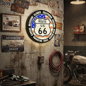 May include: A circular, illuminated wall sign featuring the Route 66 shield logo centered over a stylized American flag background. The black border lists the states of Missouri, Illinois, California, Arizona, New Mexico, Texas, Oklahoma, and Kansas.
