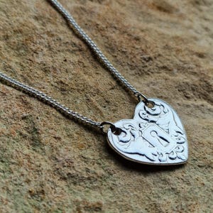 May include: A silver heart-shaped pendant necklace. The pendant features a keyhole design with ornate detailing. The necklace chain is a delicate silver. The pendant is approximately 2.5 cm wide.