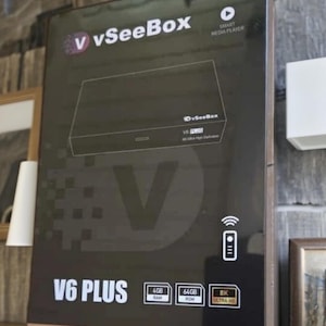 Puede incluir: Caja negra "vSeeBox V6 PLUS" con el texto "SMART MEDIA PLAYER". Presenta un gráfico de reproductor multimedia e iconos para 4 GB de RAM, 64 GB de ROM y 8K Ultra HD. Diseño moderno.