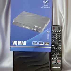 May include: A V6 MAX smart media player box with a remote control. The box is blue and black, with the brand name "vSeeBox" and the text "SMART MEDIA PLAYER". The remote is gray with multiple buttons. The box also has the specifications: 4GB RAM, 64GB ROM, and 8K Ultra HD.