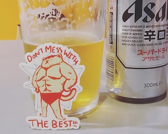 May include: A white sticker with a cartoon cat wearing red underwear and the text "Don't mess with the best!"  The sticker is on a glass of beer next to a can of Asahi Super Dry beer.