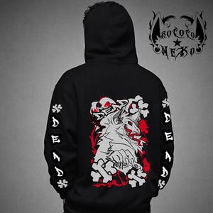 Puede incluir: Una sudadera negra con capucha que presenta un gr&aacute;fico en la espalda de una criatura blanca con detalles en rojo y la palabra DEAD. Las mangas muestran la palabra DEAD verticalmente con iconos de huesos. Un logo con el texto KOROTO NEXO aparece.