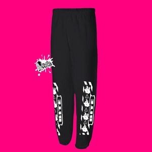 May include: Black sweatpants featuring a white graphic design. The design includes the word "BITE" in a vertical block, a cartoon face, and warning symbols. The sweatpants have an elasticated waistband.