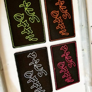 May include: Four black fabric patches with white, green, orange, and pink stitching. Each patch has the text "DAYS OFF!" written in a stylized font.