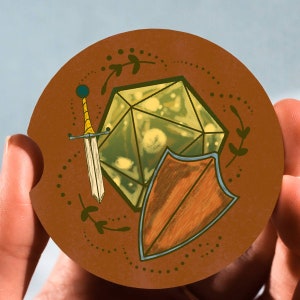 May include: A brown circle featuring a green and yellow geometric shape, a sword, and a shield. The geometric shape is a 20-sided die, also known as a d20. The sword has a gold handle and a blue blade. The shield is brown with a blue border.