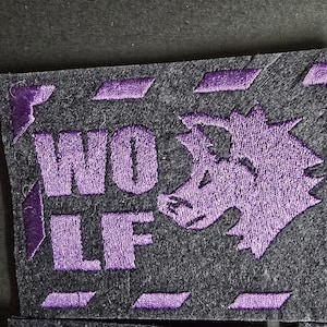 May include: Purple embroidered patch featuring the word "WOLF" and a stylised wolf design on a dark grey background.