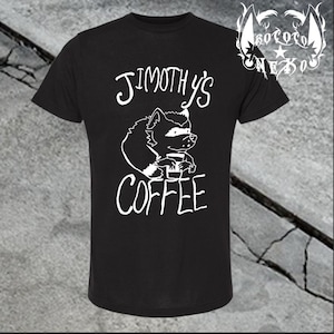 May include: A black short-sleeved t-shirt featuring a white graphic of a raccoon holding a coffee cup. The text above the raccoon reads "JIMOTHY'S" and the text below reads "COFFEE". A small logo with the text "KOKORO NEKO" is in the top right corner.