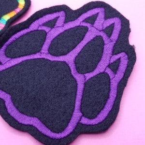 May include: Purple paw print embroidered on a black felt patch.