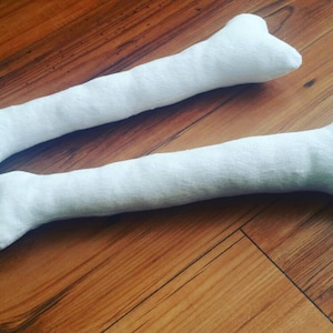 May include: Two white plush bone-shaped dog toys. The toys are made of soft, white fabric and are about 30 cm long.