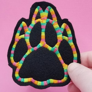 May include: A black felt paw print patch with a colourful striped border. The border is made of pink, orange, green and yellow thread.
