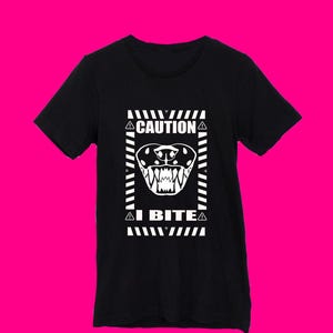 May include: Black t-shirt featuring a white graphic of a warning sign that reads "CAUTION I BITE" with a cartoon image of a dog's mouth with sharp teeth.